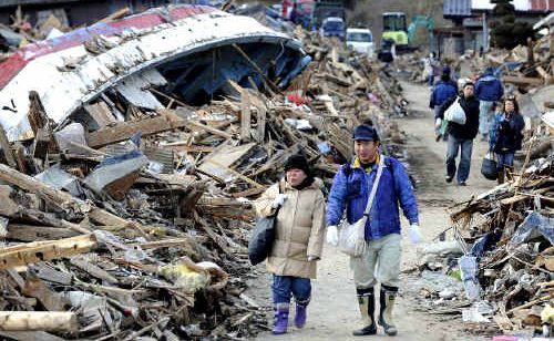 DAZED: Residents of Minamisanriku, in Miyagi prefecture, walk through debris, including an overturned boat, a day after the tsunami hit. DAZED: Residents of Minamisanriku, in Miyagi prefecture, walk through debris, including an overturned boat, a day after the tsunami hit.